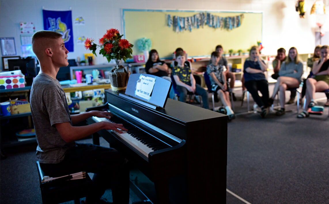 Student playing the piano for other students