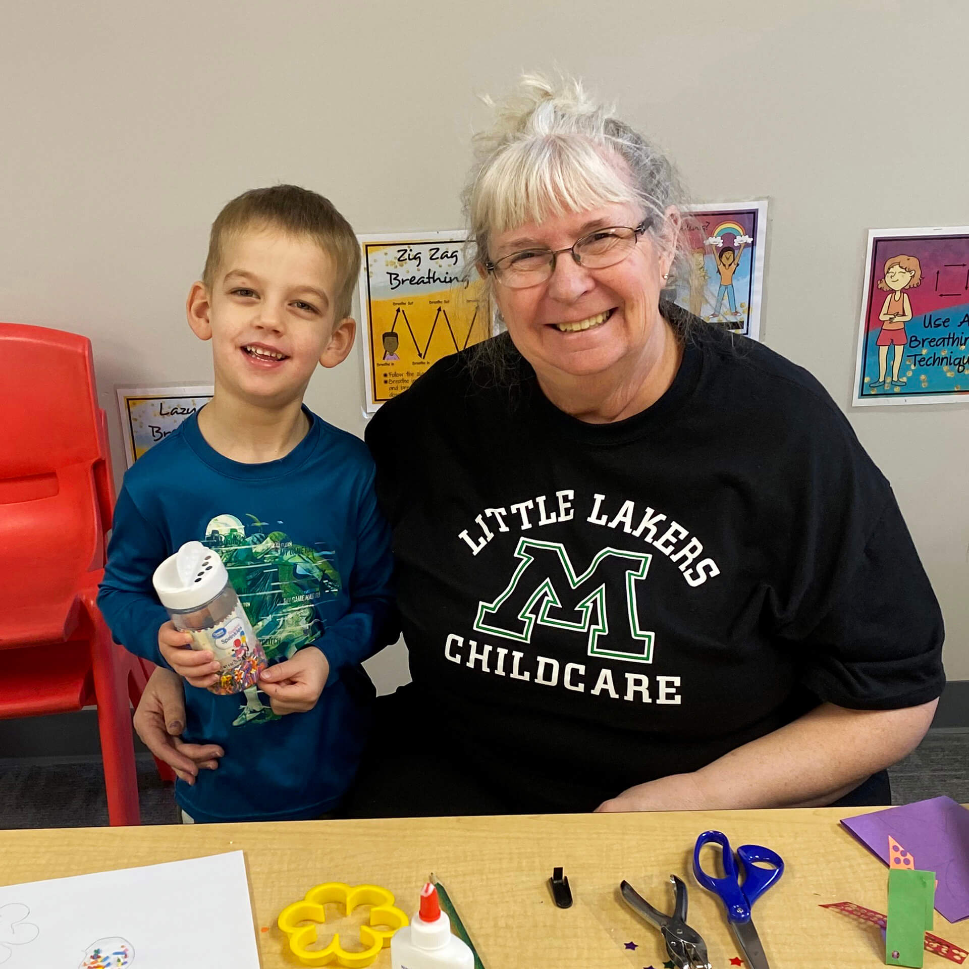 Child care provider posing with child at craft table