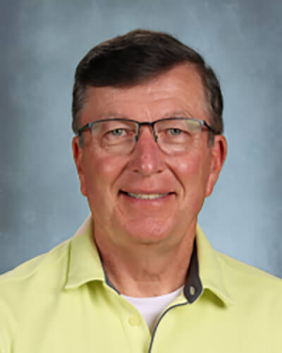 Portrait of a male with short brown hair wearing glasses in front of a gray background
